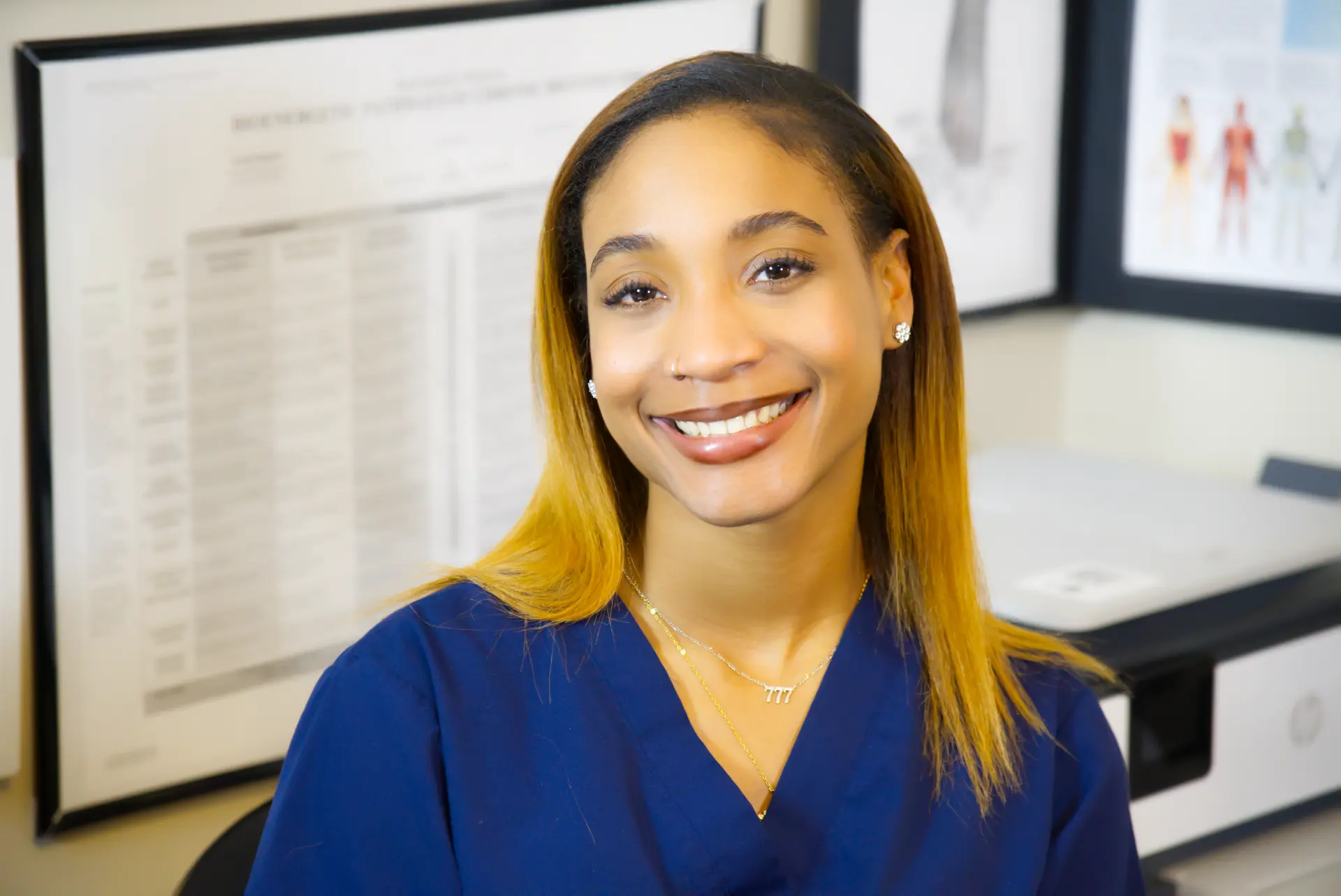 Jade Davis smiling in the office, anatomical charts behind her